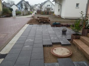 Pflasterarbeiten an einer Hauseinfahrt im Kreis Rastatt beim Verlegen dunkler Pflastersteine auf einem Splittbett.