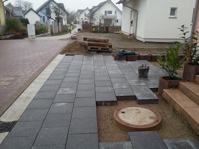 Pflasterarbeiten an einer Hauseinfahrt im Kreis Rastatt beim Verlegen dunkler Pflastersteine auf einem Splittbett.